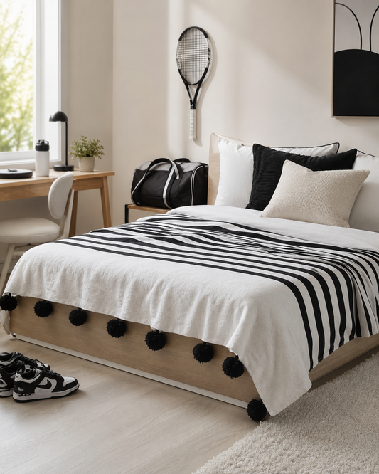 VVC black and white organic cotton blanket handmade in Morocco, styled as a large bed throw with black pompoms, available at VVC SHOP Sitia Crete and viktoria-vigh.com