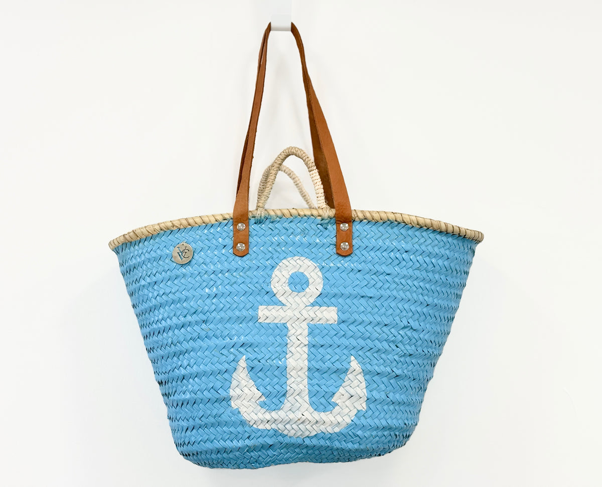 Front view of a handmade VVC™ blue beach basket with white anchor design and leather handles. Spacious shopping tote and beach bag inspired by Mediterranean coastal living.