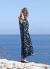 Front-side view of a woman wearing the VVC blue-and-black floral sequin mullet dress on a rocky coastline.