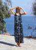 Rear-side view of the VVC blue-and-black floral sequin mullet dress showing its dramatic long back hem beside the sea.