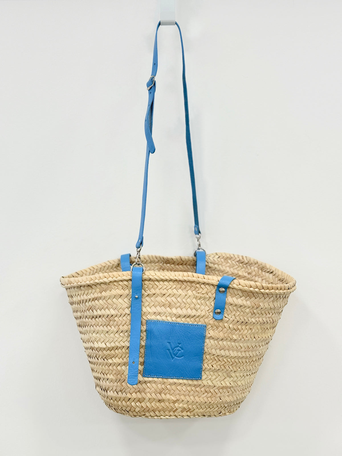Front view of handmade VVC™ palm leaf crossbody basket with blue leather pocket and adjustable shoulder strap. Lightweight shopping bag and beach basket available in Sitia, Crete.
