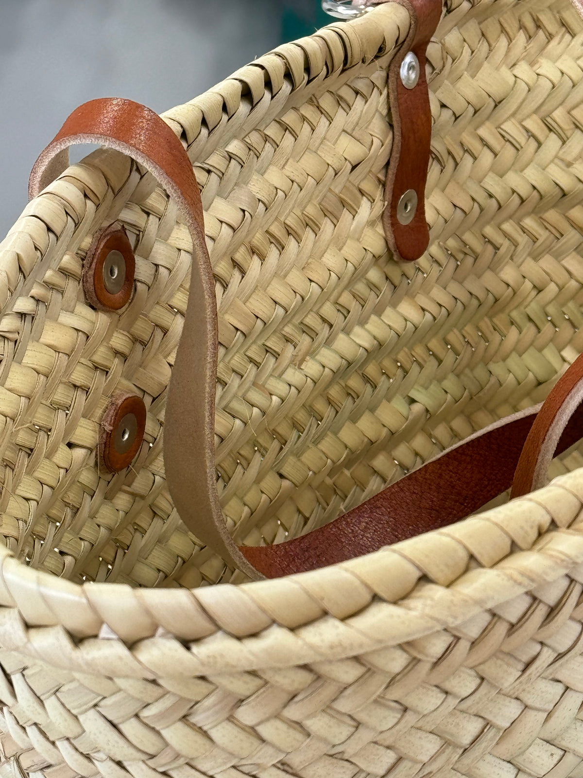 Close-up of the handmade VVC™ crossbody basket showing premium brown leather strap attachment and traditional woven palm leaf craftsmanship.