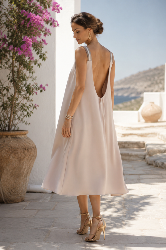 Back view of the VVC flowing blush low-back midi dress with a soft A-line silhouette in a Greek island setting.