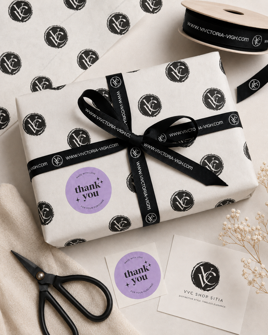 VVC gift wrapping flat lay with branded paper, black ribbon, thank you stickers and boutique packaging details for VVC SHOP Sitia, Crete.
