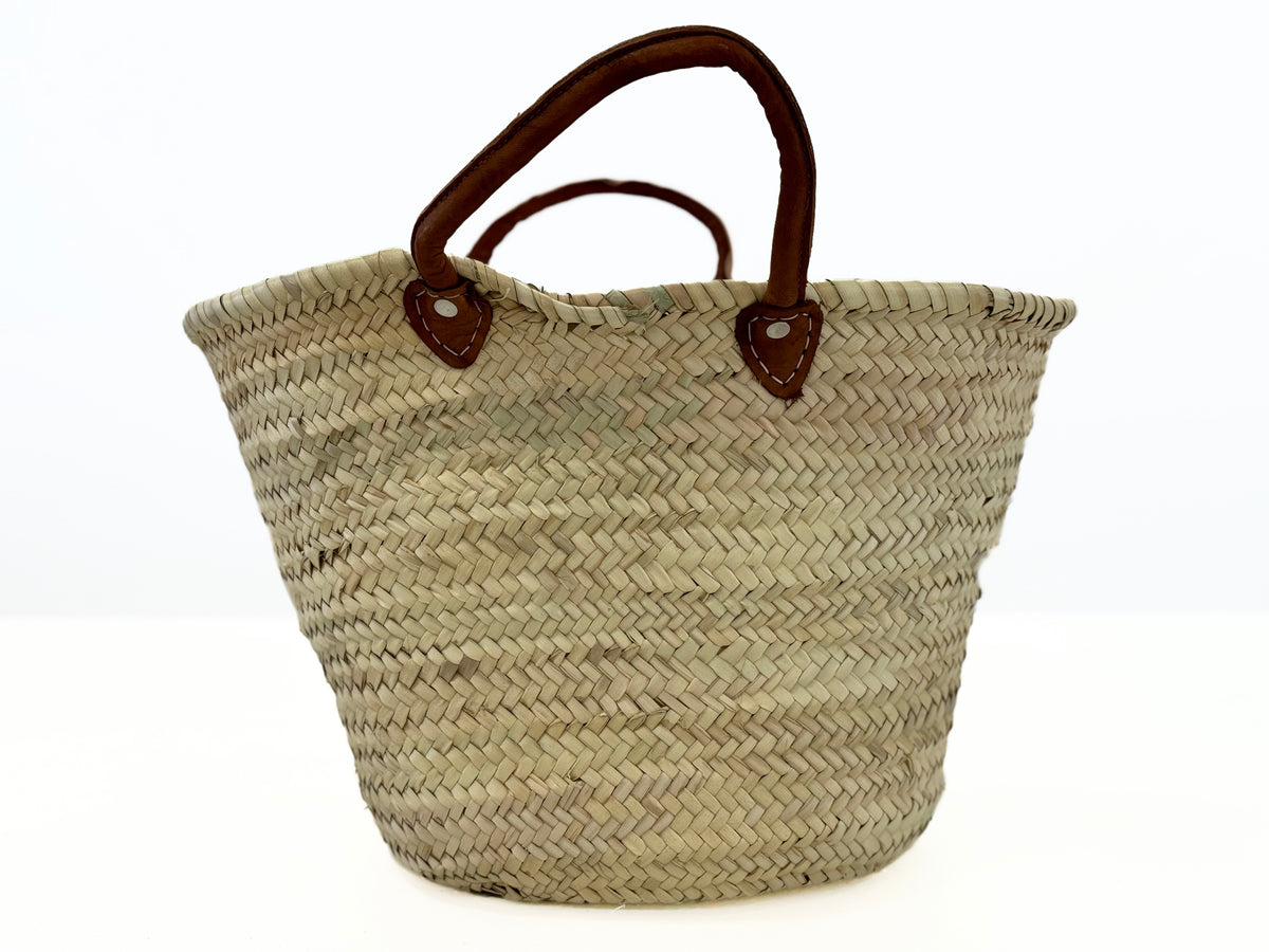 Large handmade palm leaf storage basket with short leather handles in a modern Mediterranean kitchen.