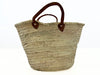 Large handmade palm leaf storage basket with short leather handles in a modern Mediterranean kitchen.