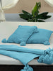 Flat lay of VVC™ turquoise organic cotton blanket showing decorative pompoms.