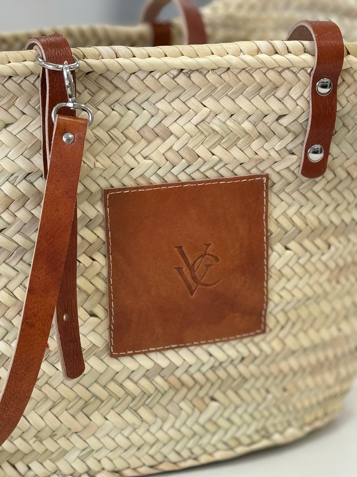 Detail view of the VVC™ handmade palm leaf basket featuring a practical brown leather pocket for mobile phone, keys and everyday essentials.