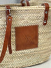 Detail view of the VVC™ handmade palm leaf basket featuring a practical brown leather pocket for mobile phone, keys and everyday essentials.
