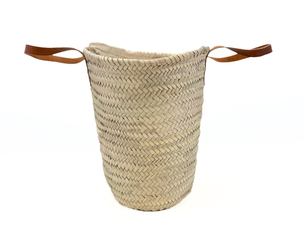 Side view of large handmade palm leaf basket with brown leather handles and natural woven raffia texture.