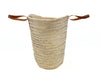 Side view of large handmade palm leaf basket with brown leather handles and natural woven raffia texture.
