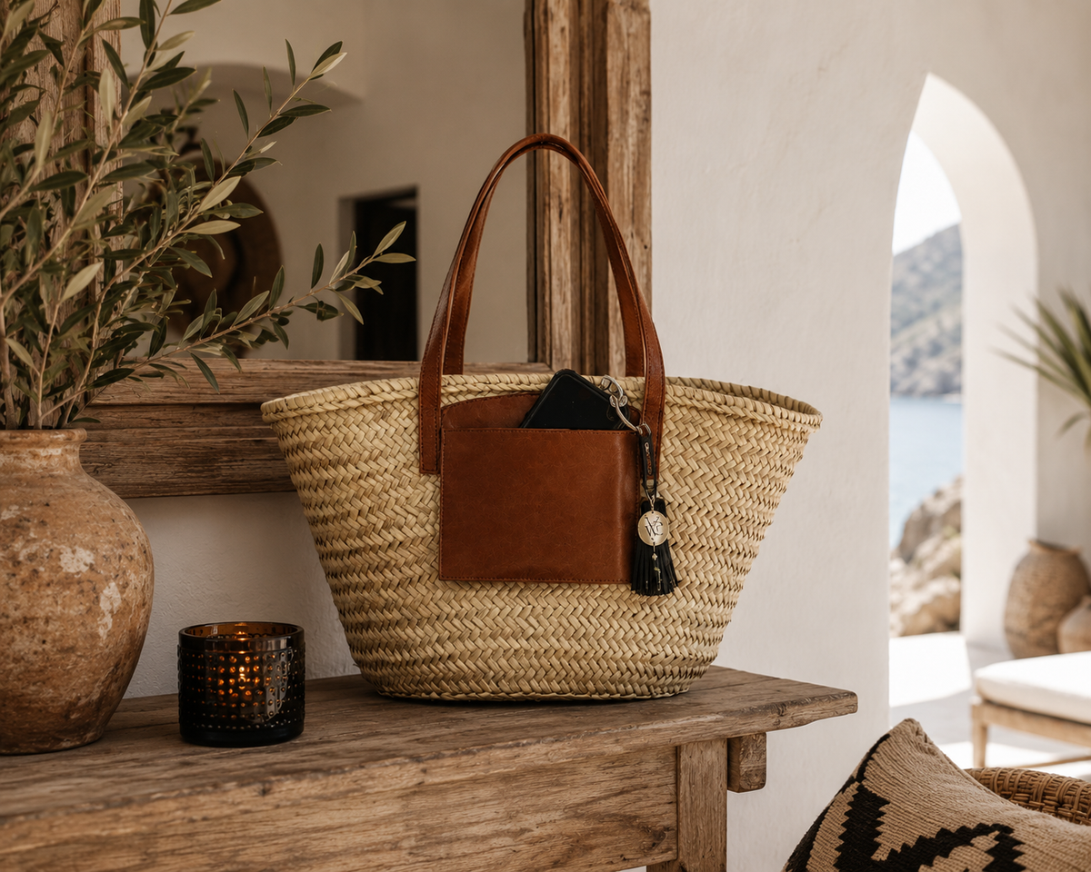 Handmade VVC™ palm leaf basket with leather handles and leather pocket styled as Mediterranean home décor on a rustic console table in Crete.