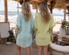 Two women wearing VVC™ zebra print beach cover-up dresses in turquoise and lime green at a luxury beach club in Crete, Mediterranean resort wear from VVC SHOP Sitia