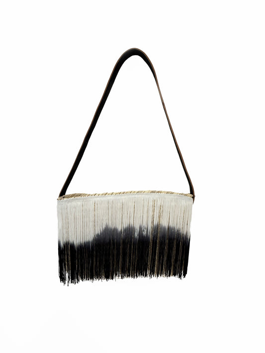 Back view of a handmade VVC raffia shoulder bag featuring long black and white ombré fringes, natural raffia construction and a leather shoulder strap.