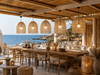 Five XXL natural raffia pendant lampshades above a wooden dining table in a boho-style Crete beach club.