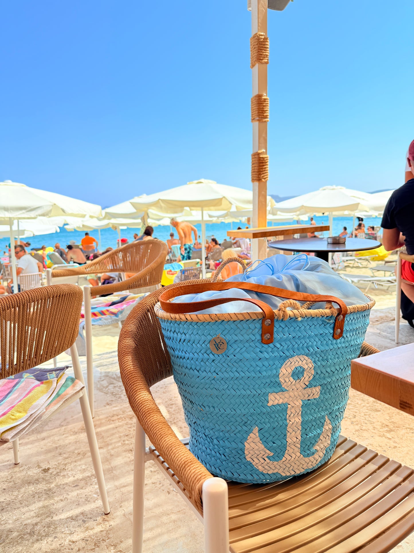 Blue woven bag with anchor design on a beach chair, with people and umbrellas in the background at the beach of sitia, crete