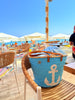 Blue woven bag with anchor design on a beach chair, with people and umbrellas in the background at the beach of sitia, crete