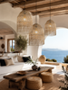 Three XXL natural raffia pendant lampshades in a bright Greek island living room with sea views, styled for VVC Shop Sitia.