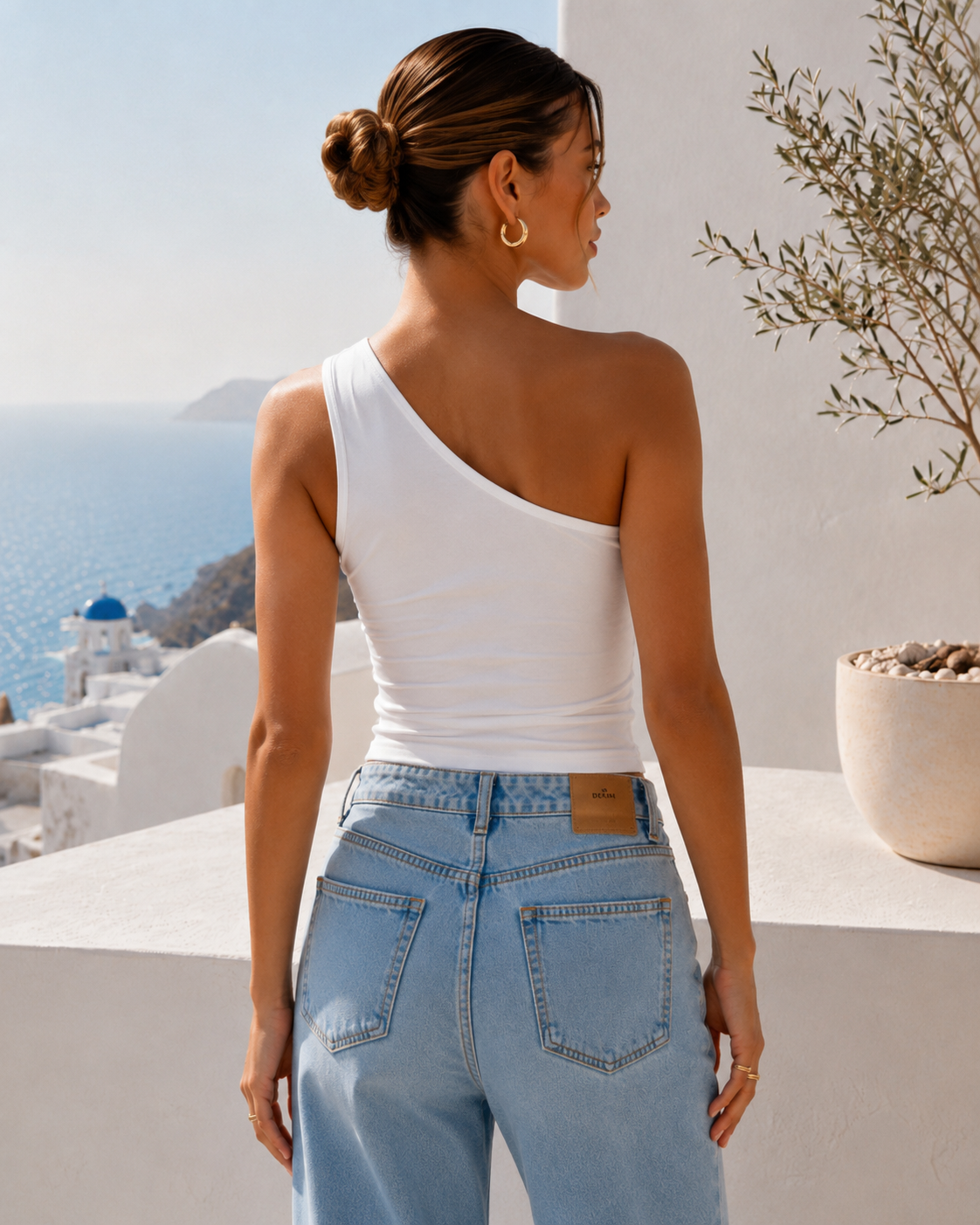 Back view of a white one-shoulder summer top showing the asymmetric shoulder design in a Mediterranean setting.