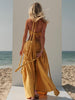 Full-length rear-side view of a woman wearing the ZOE Zena mustard-yellow cotton-crepe halter top and matching maxi-skirt set beside the sea.