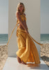 Full-length side view of a woman wearing the ZOE Zena mustard-yellow halter top and flowing maxi-skirt set beside the sea.